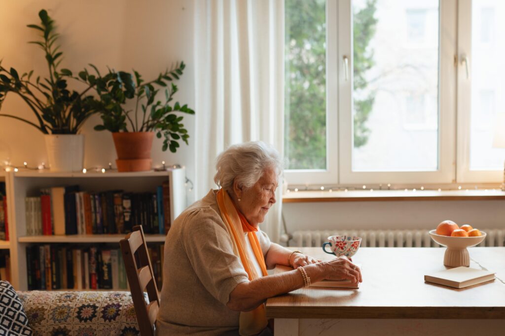 Einsame Seniorin sitzt allein am Tisch und liest – Herztat unterstützt einsame Senioren